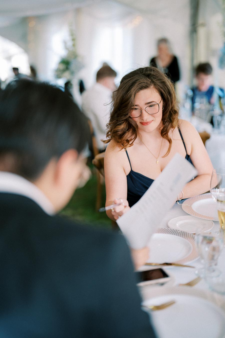 A woman in glasses reading a menu at an elegantly set table during a formal event.