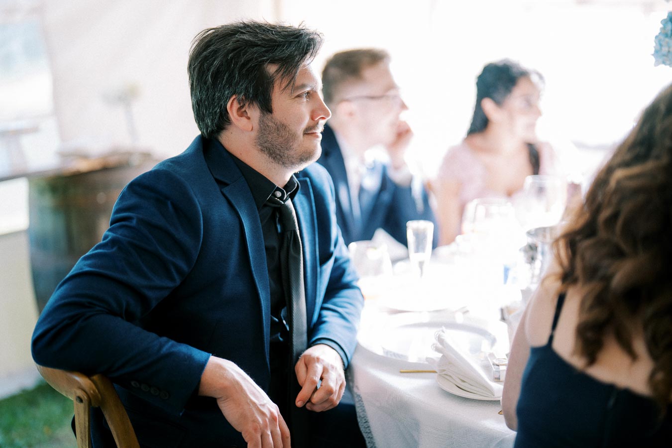 A man in a blue suit sits at a decorated table during a formal event, surrounded by other guests, creating a festive atmosphere.