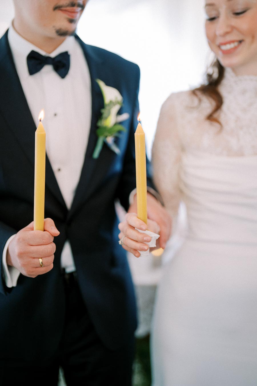 A bride and groom holding lit candles during their wedding ceremony, symbolizing unity and love, dressed in elegant wedding attire.