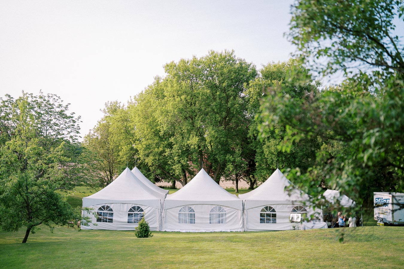 White event tents set up in a lush green outdoor setting, surrounded by trees and open space, ideal for weddings or gatherings.