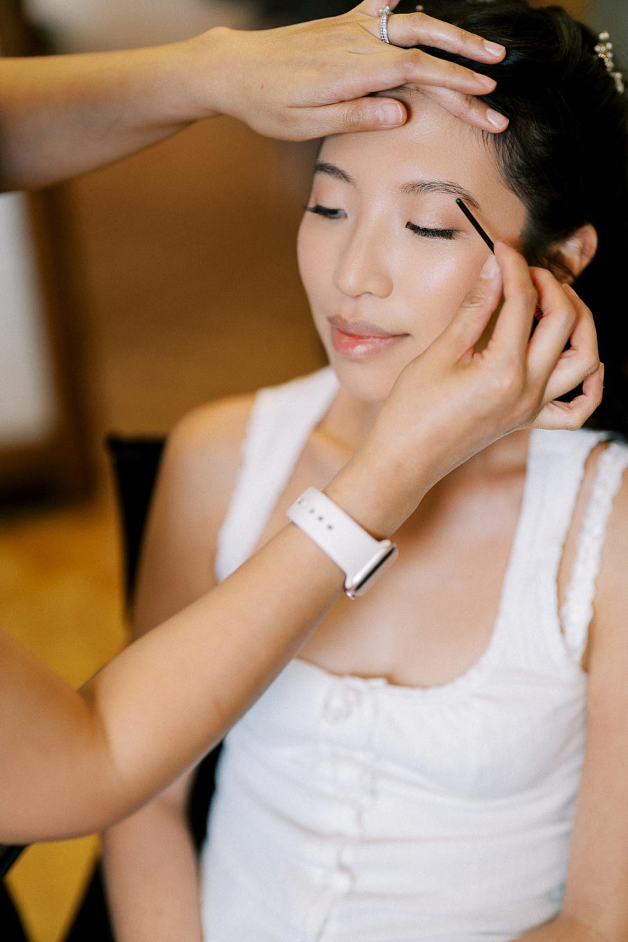 A makeup artist applying eyeshadow on a woman's eyelid, creating a natural bridal look.