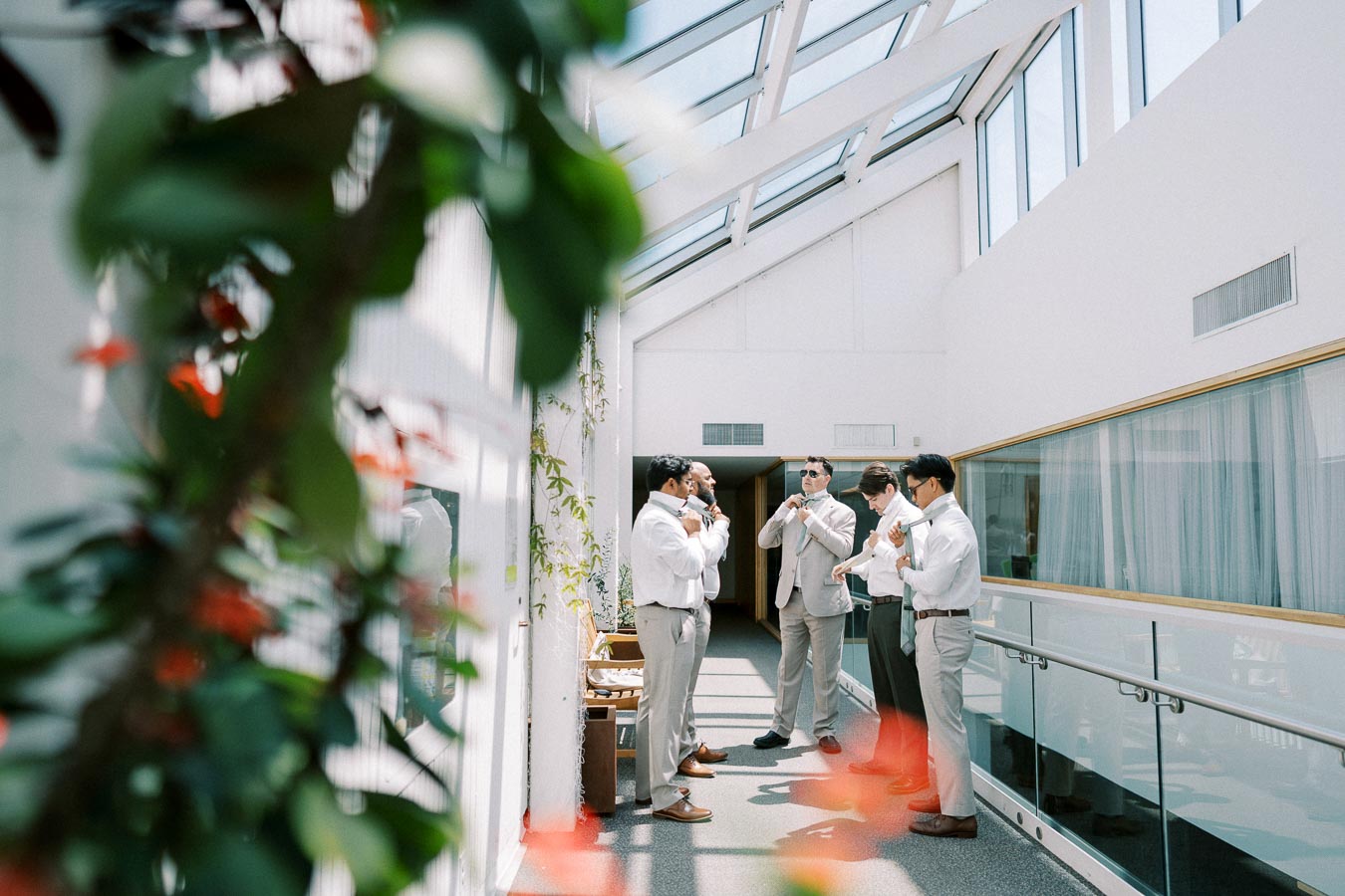 A group of men preparing for an event in a bright, modern hallway with glass ceilings.