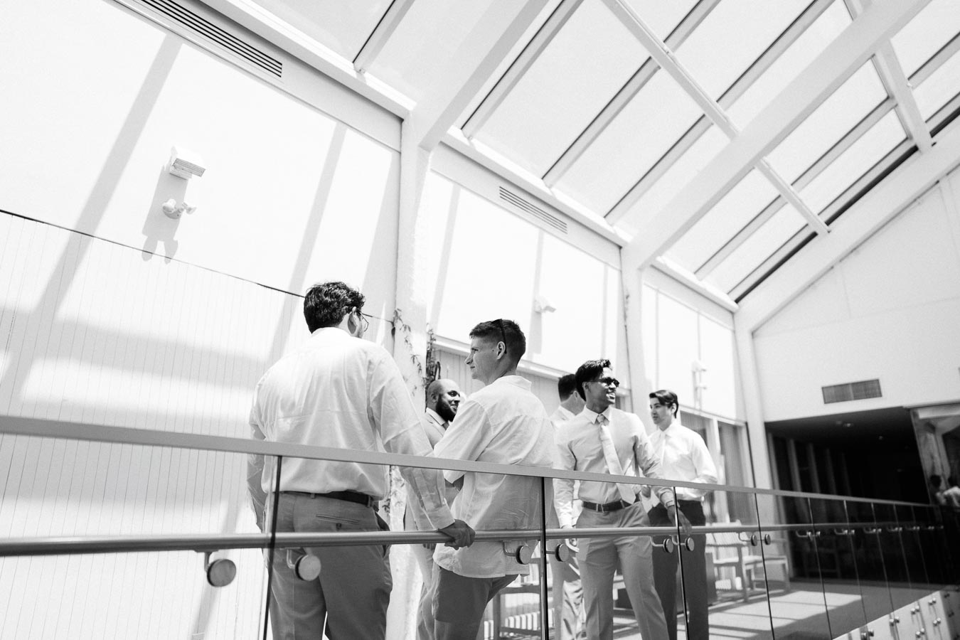 A group of men talking and enjoying a conversation in a sunlit building with modern architecture, featuring large windows and a bright, airy atmosphere.