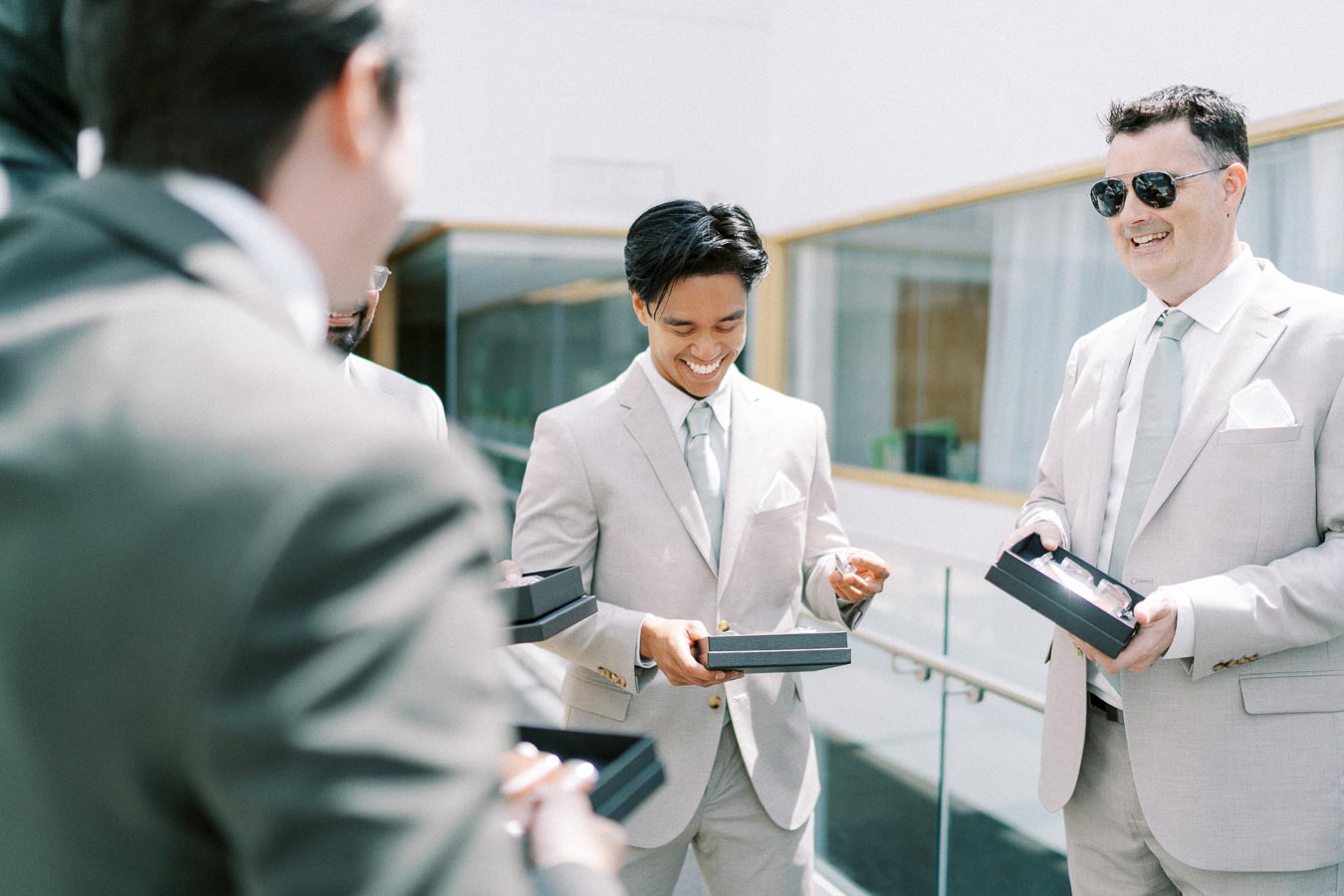 Group of men in light suits sharing a joyful moment while exchanging gifts in a bright, modern indoor setting.