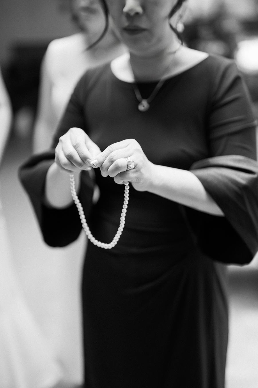 A woman in a black dress holding a pearl necklace, showcasing elegance and timeless style in a monochrome setting.