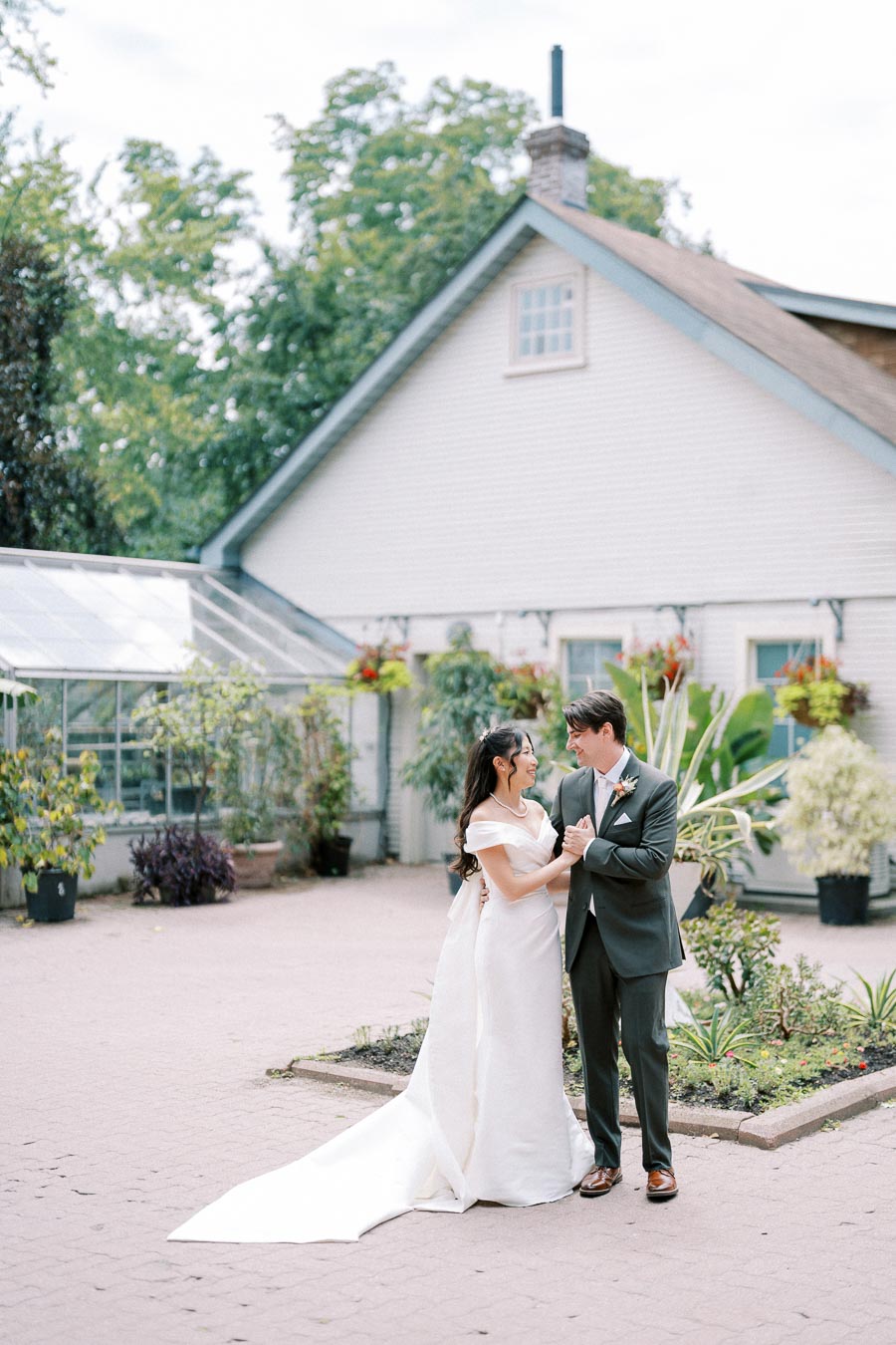 Outdoor wedding photoshoot featuring a happy couple in elegant attire standing in front of a picturesque house with lush greenery.