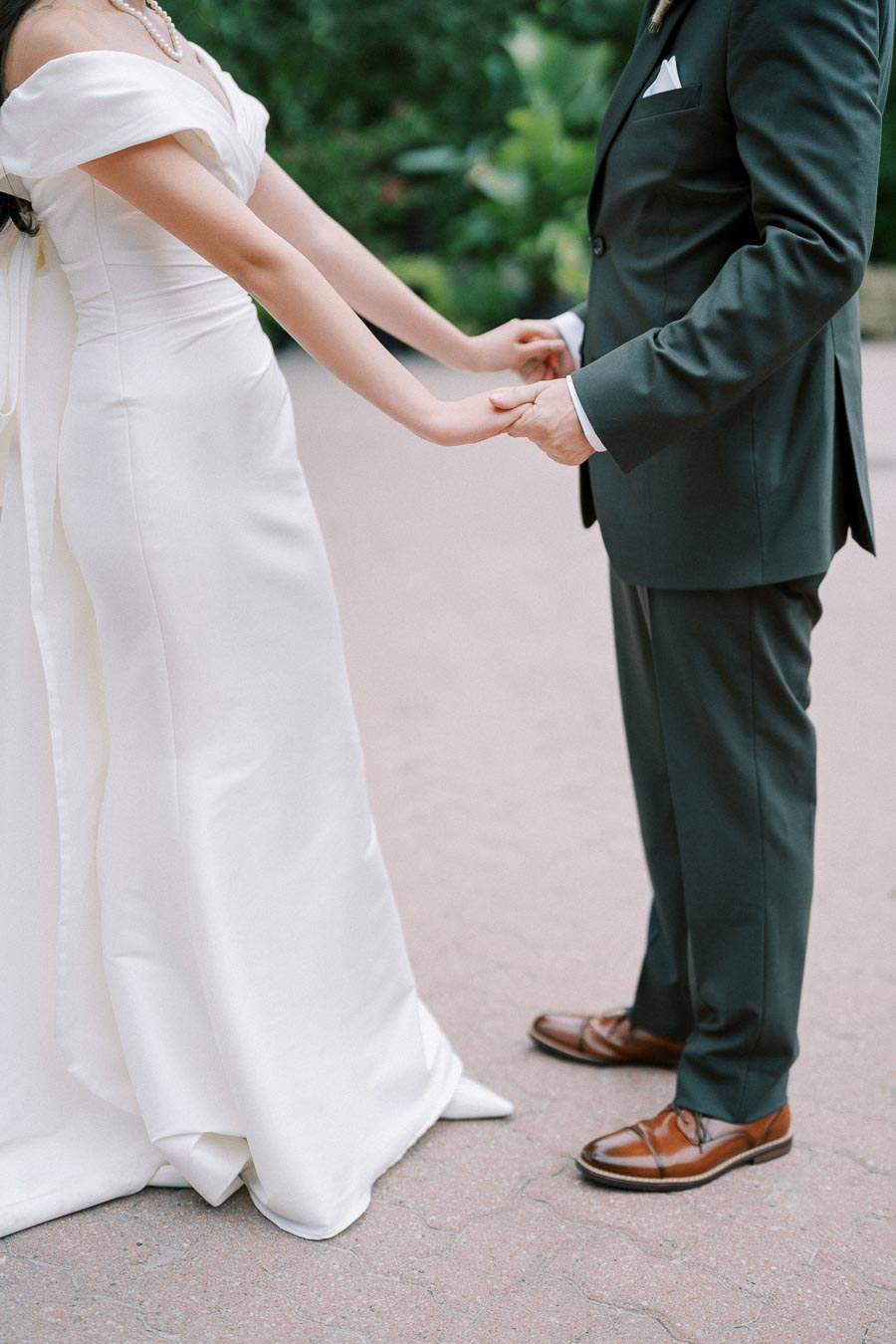 A bride and groom holding hands during an outdoor wedding ceremony, bride in a white dress and groom in a dark suit, showcasing elegant wedding attire.