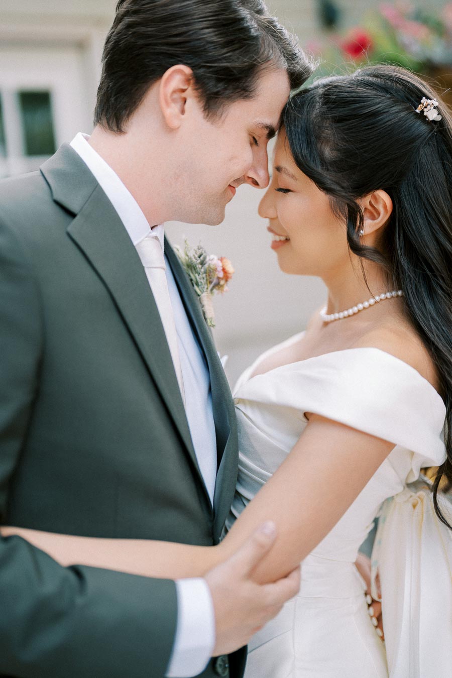 Romantic wedding couple embracing, bride in off-shoulder gown and groom in suit, sharing intimate moment outdoors.