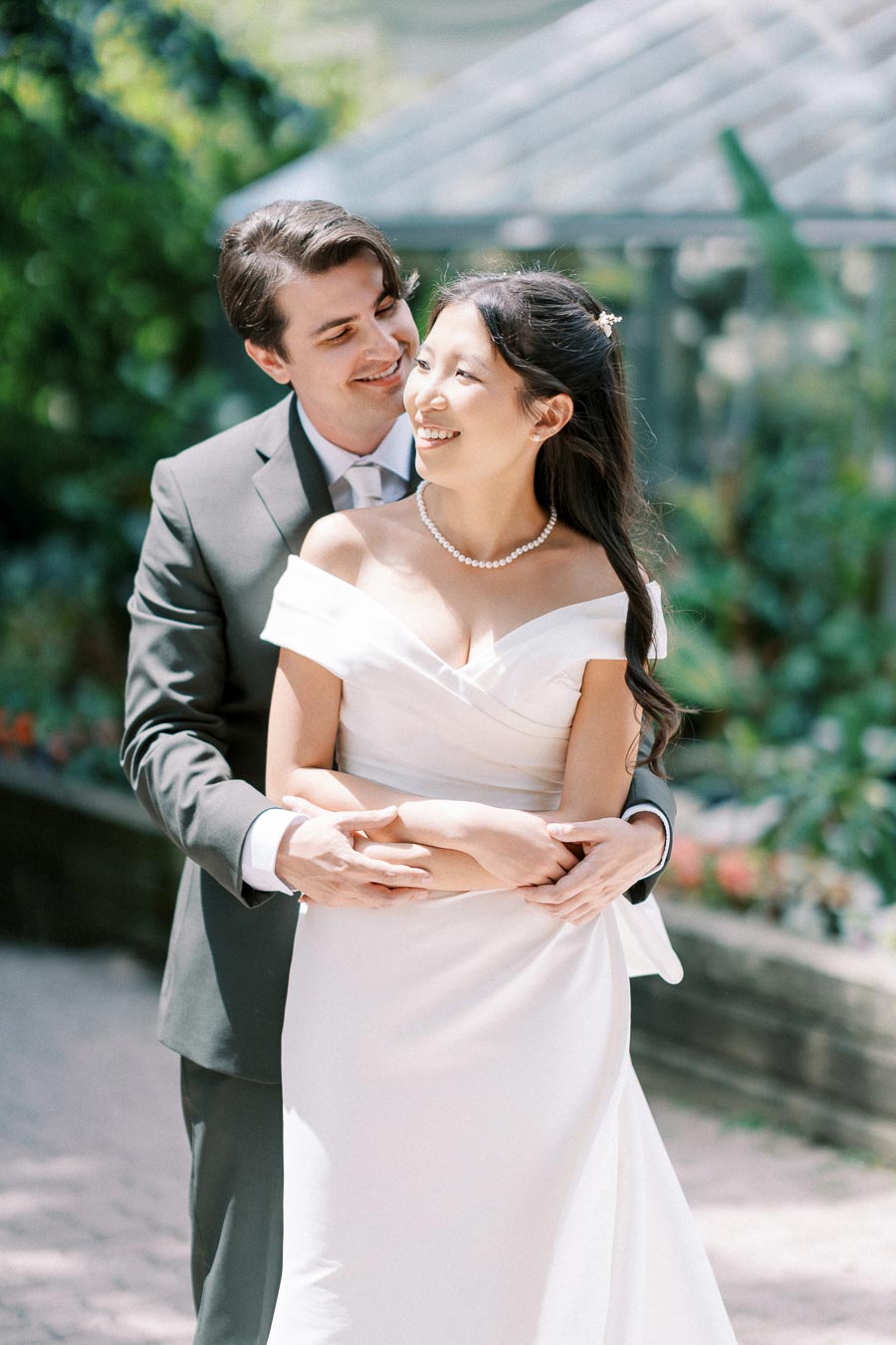 A happy couple embracing on their wedding day, the bride in an elegant white gown and the groom in a dark suit, smiling in a lush garden setting.