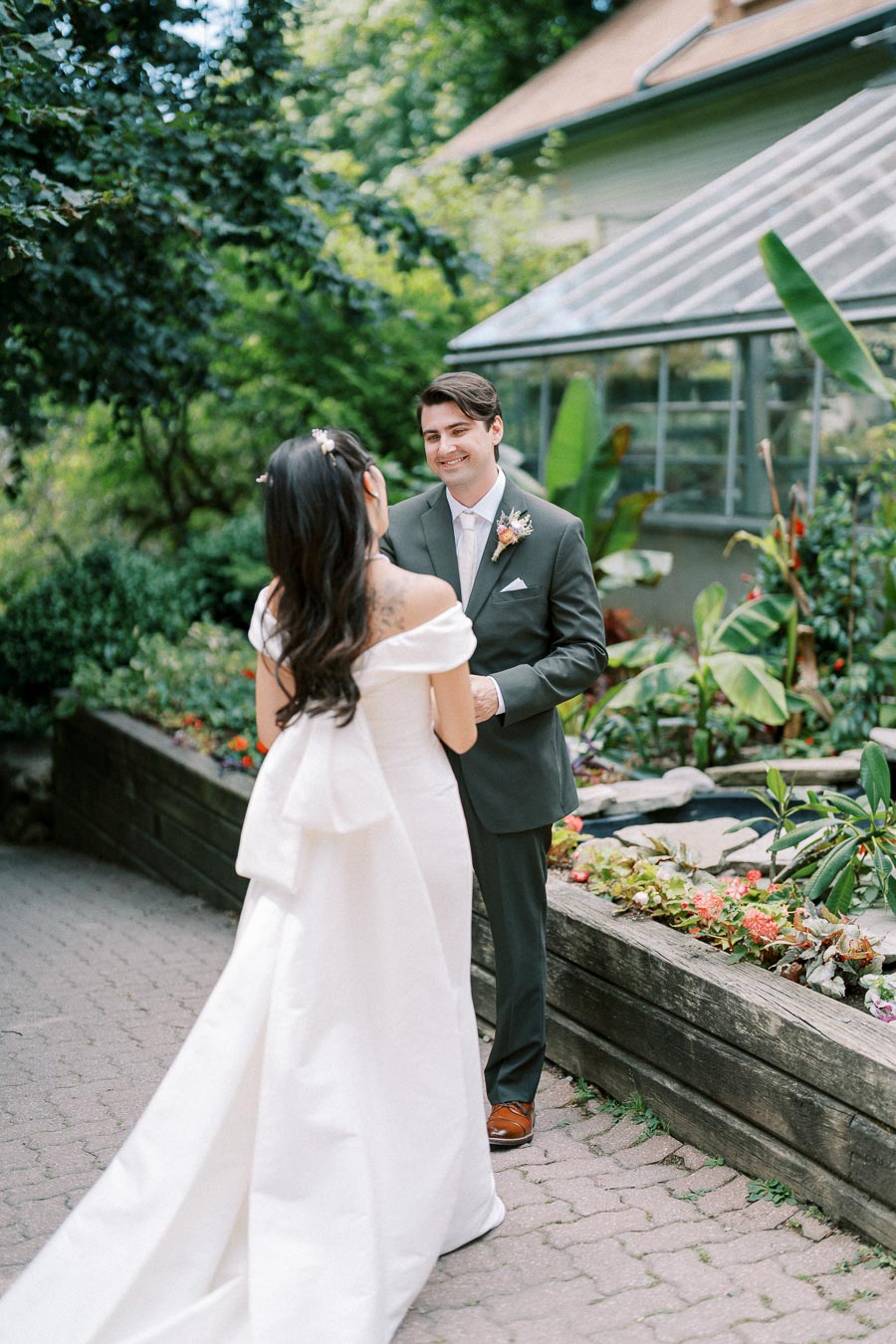 A couple in elegant wedding attire shares a joyful moment in a colorful garden setting, with lush greenery and floral arrangements surrounding them.