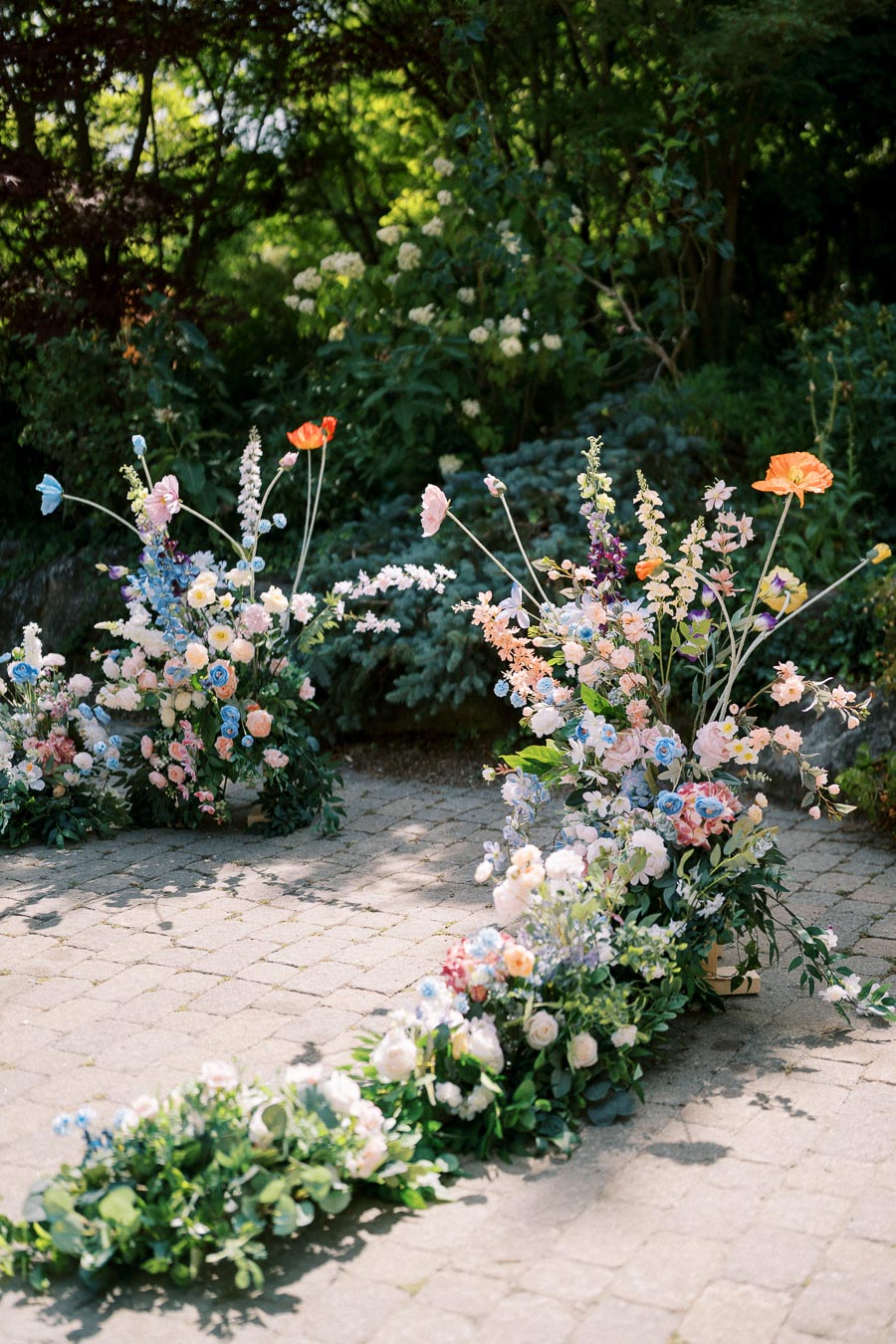 Colorful garden wedding flower arrangements featuring pastel blooms and greenery on a sunlit cobblestone path.