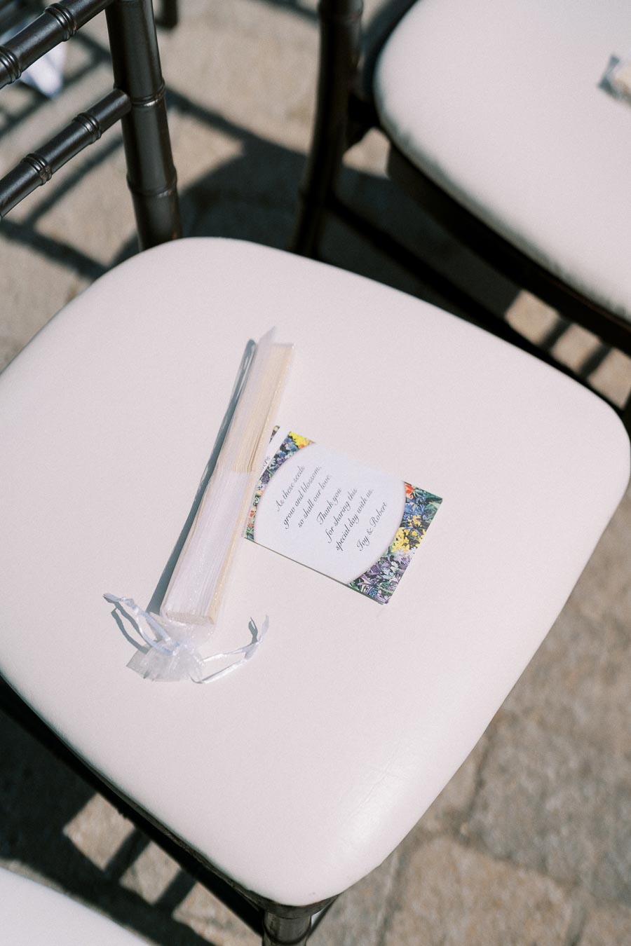 White cushioned chair with a program and bamboo fan, wedding ceremony setting.