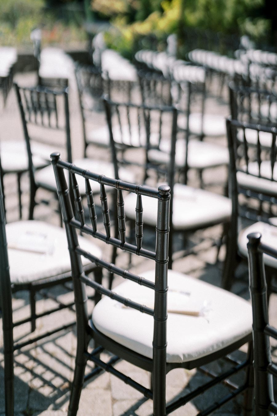 Empty black chiavari chairs set up for an outdoor wedding ceremony on a sunny day.