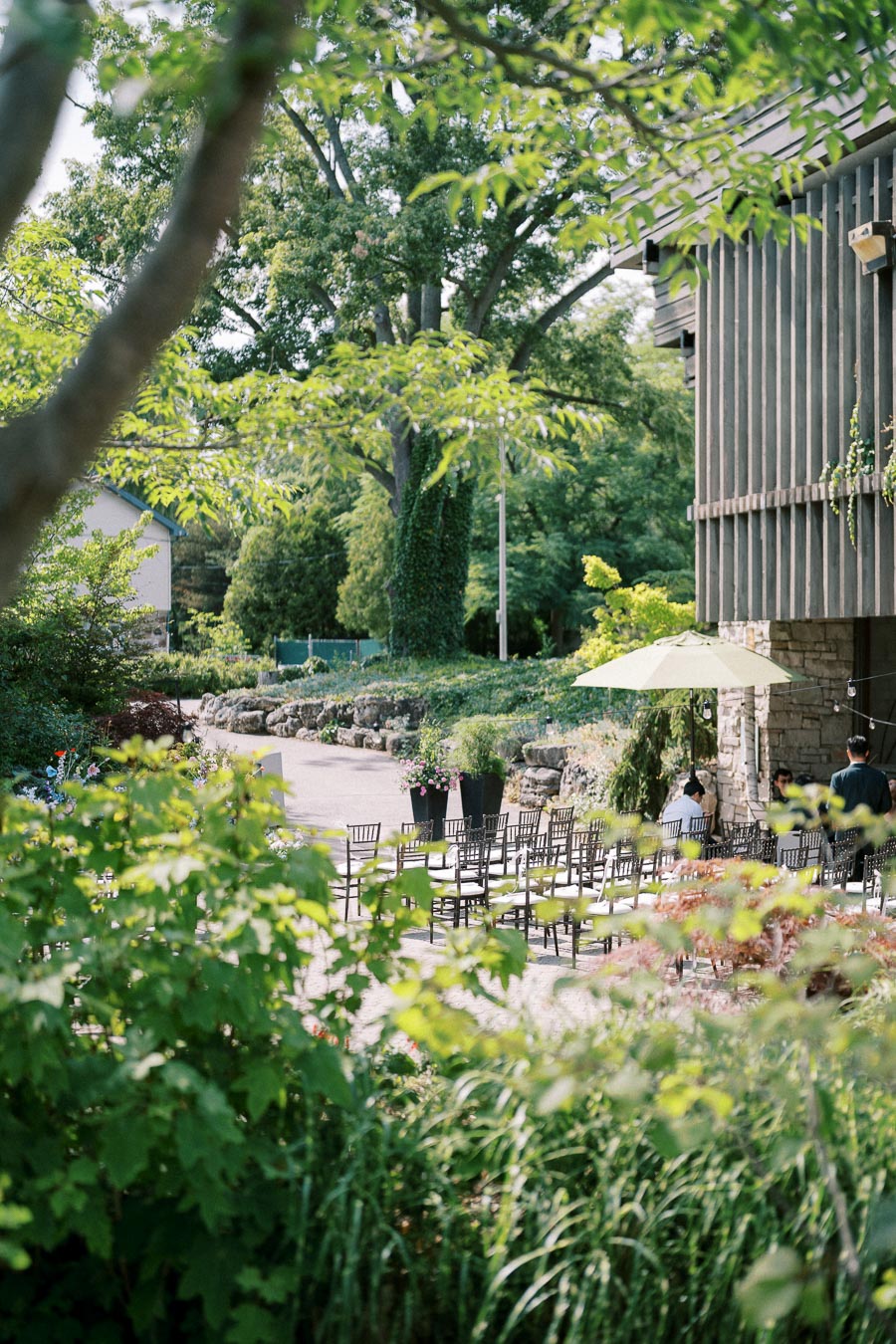 A scenic outdoor wedding venue with rows of chairs under lush green trees and a rustic building, perfect for a natural and serene ceremony setting.