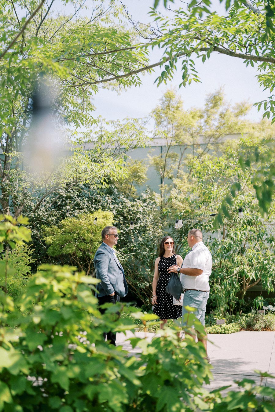 Three people having a conversation outdoors surrounded by lush greenery on a sunny day.