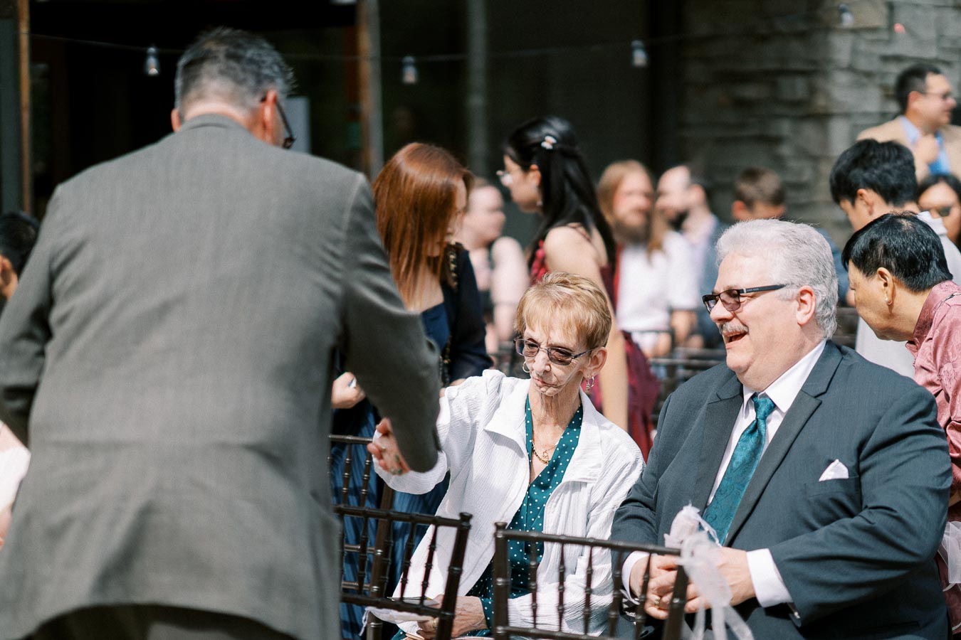Guests interacting at an outdoor event, with a man in a suit greeting an elderly woman.