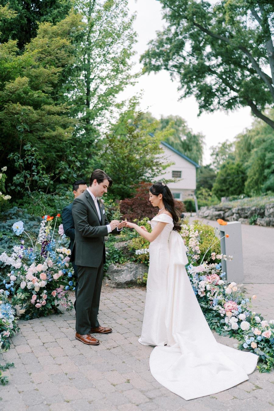 A bride and groom exchanging rings during an outdoor wedding ceremony, surrounded by lush greenery and colorful flowers.