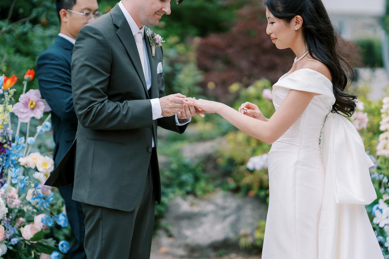 A bride and groom exchanging rings during their outdoor wedding ceremony, surrounded by colorful flowers.