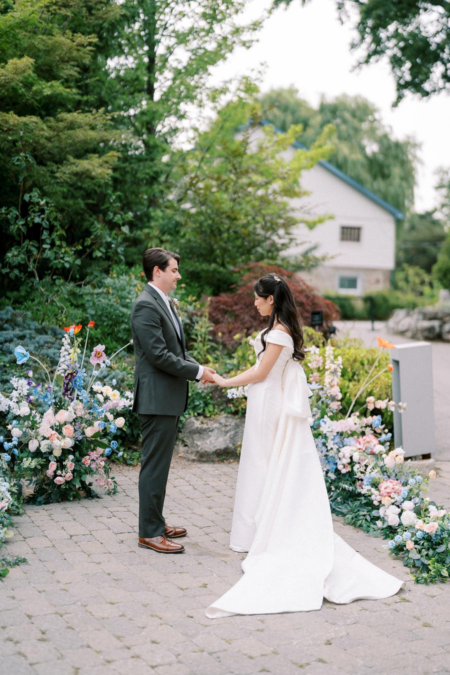 Bride and groom holding hands in a lush garden setting, surrounded by colorful flowers, on their wedding day.