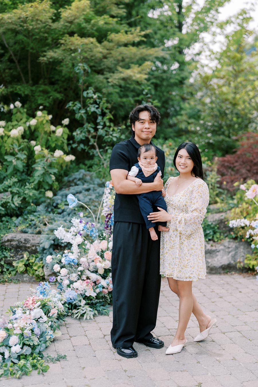 A family posing in a garden setting with lush greenery and colorful floral arrangements, displaying happy expressions.
