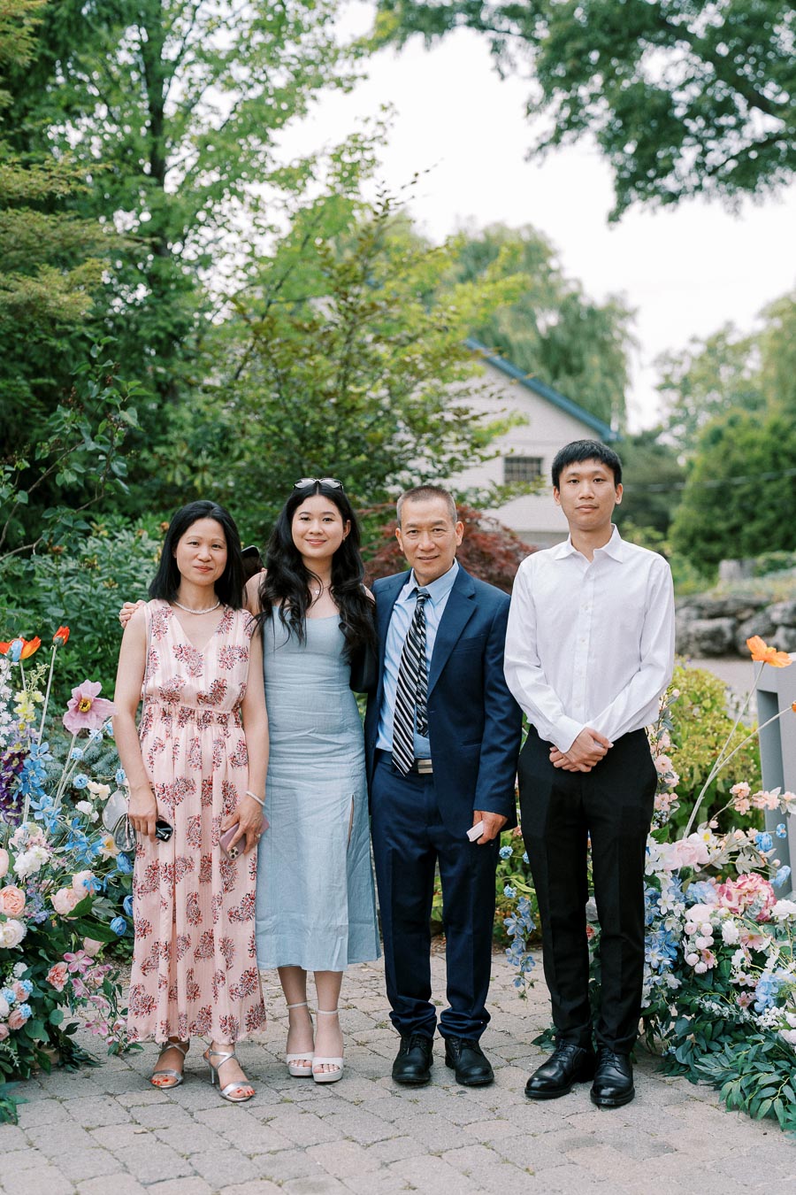 Family posing together outdoors in a garden setting with colorful flowers and lush greenery.