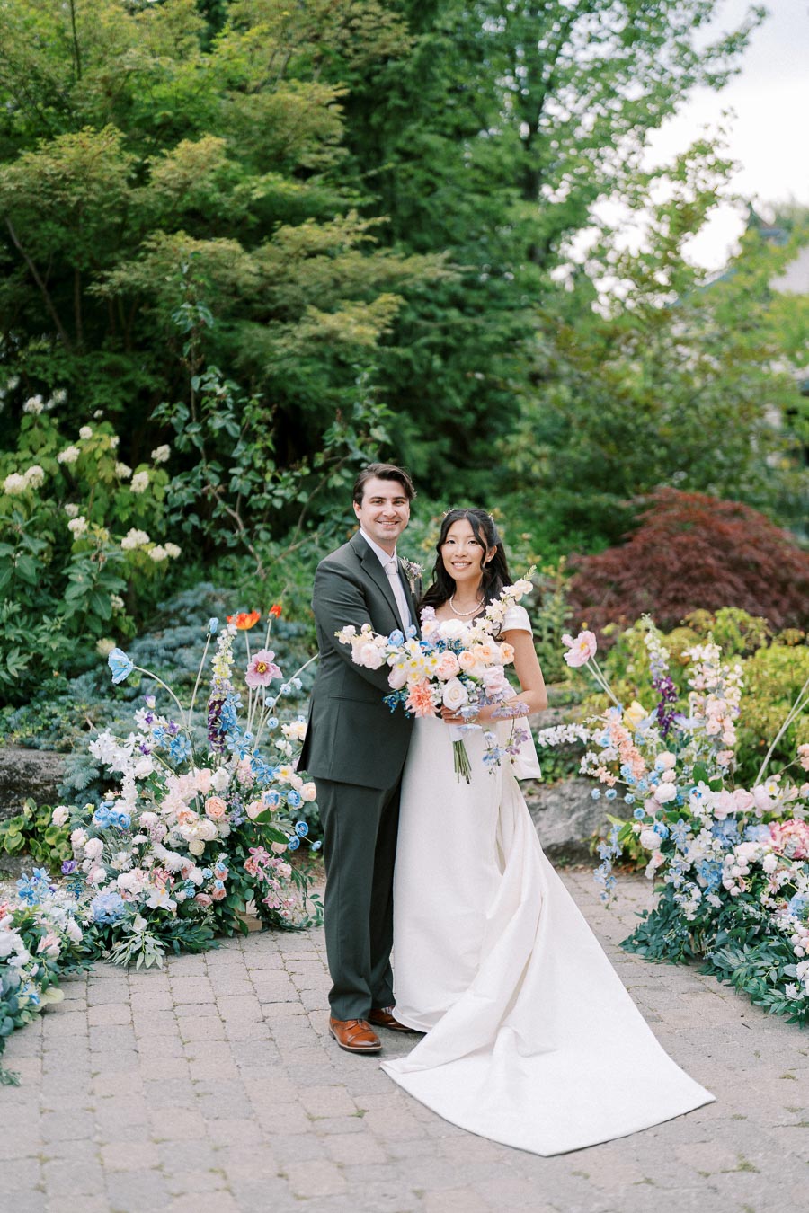 A joyous bride and groom pose with colorful floral arrangements in a lush garden setting, capturing a perfect wedding moment.