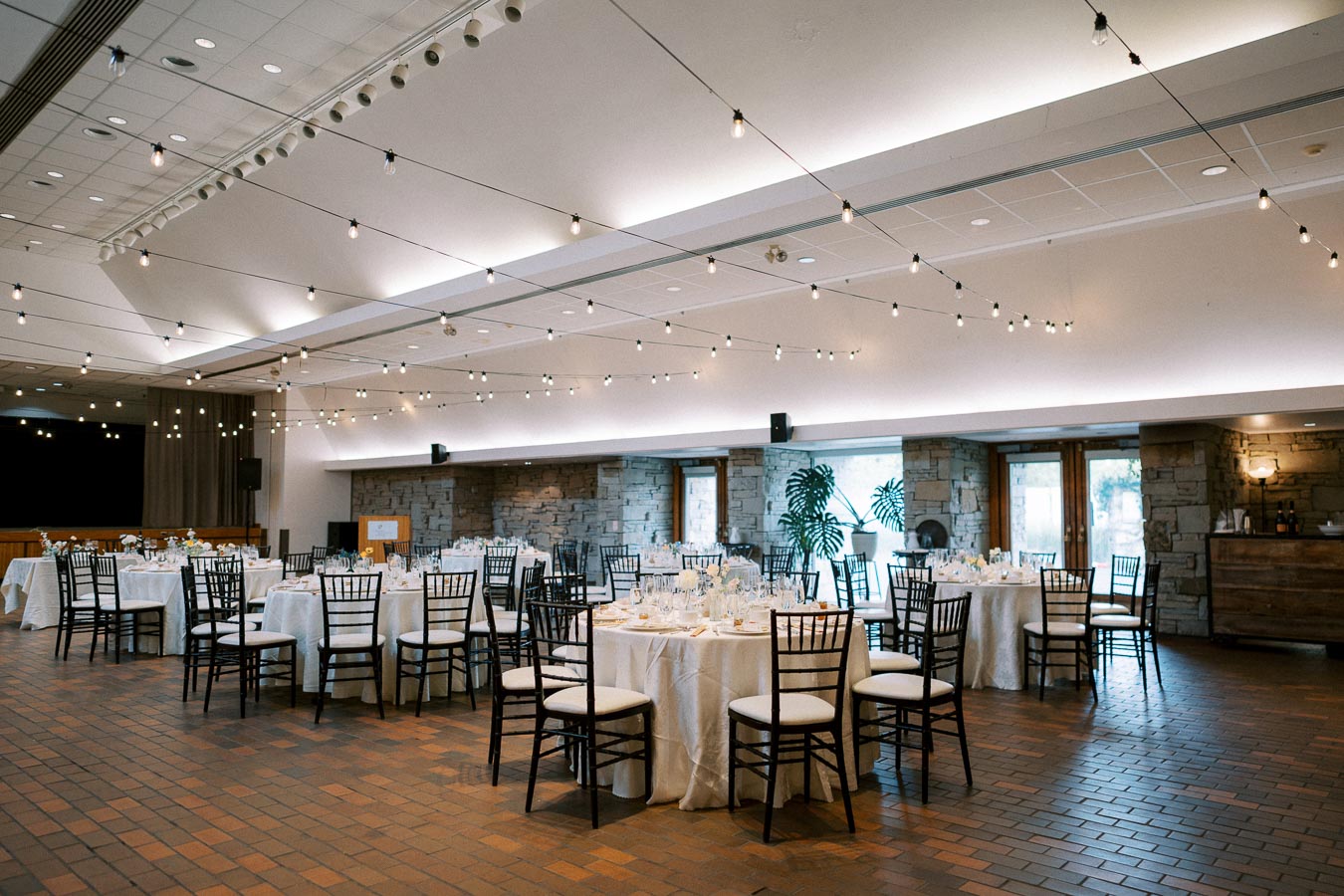 Elegant banquet hall with round tables set for an event, featuring string lights and modern decor.