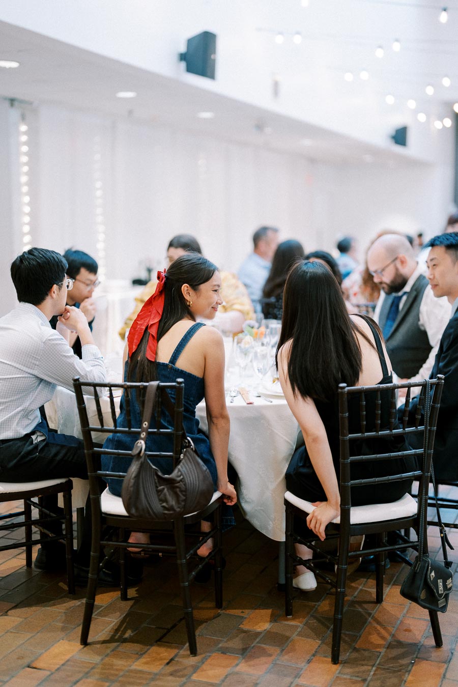 A group of people sitting at a round table during an indoor event, engaged in conversation and enjoying the gathering in a bright, elegantly decorated space.
