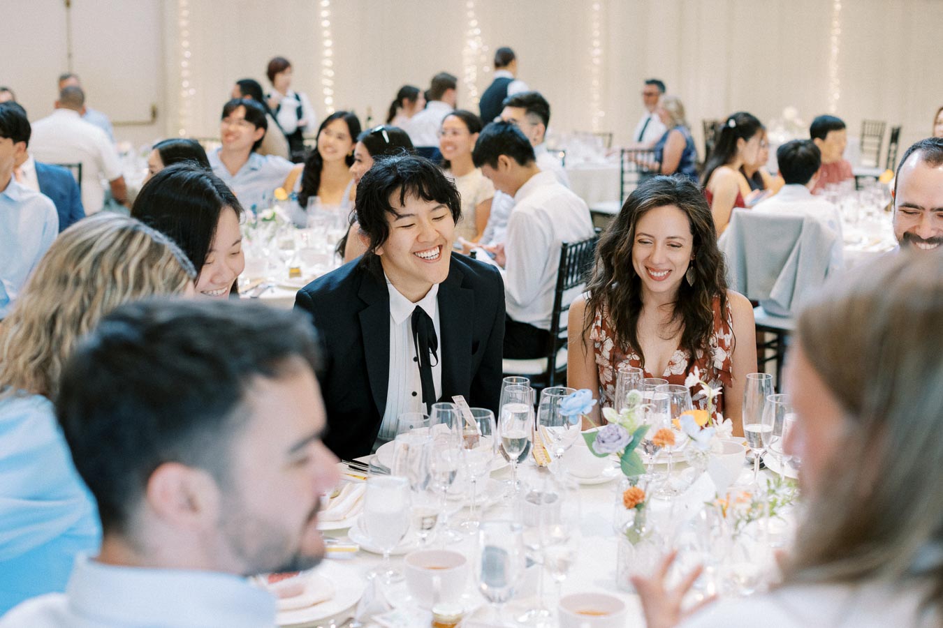 A diverse group of people smiling and enjoying a formal gathering at a beautifully decorated banquet table, featuring floral centerpieces and elegant tableware.