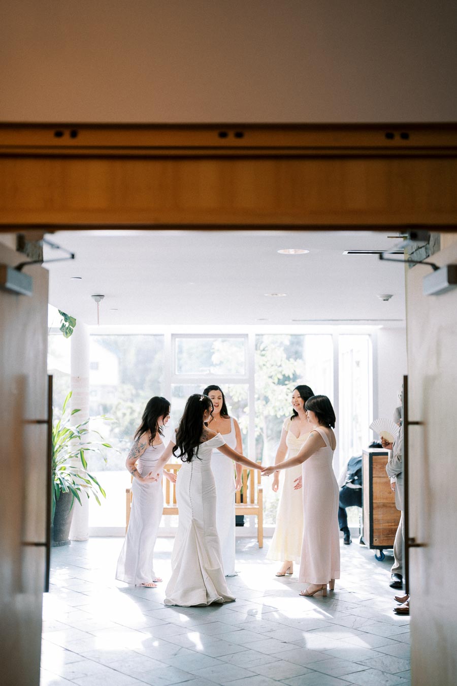 Bridal party in pastel dresses sharing a joyful moment indoors, showcasing bridesmaids and the bride in natural light.