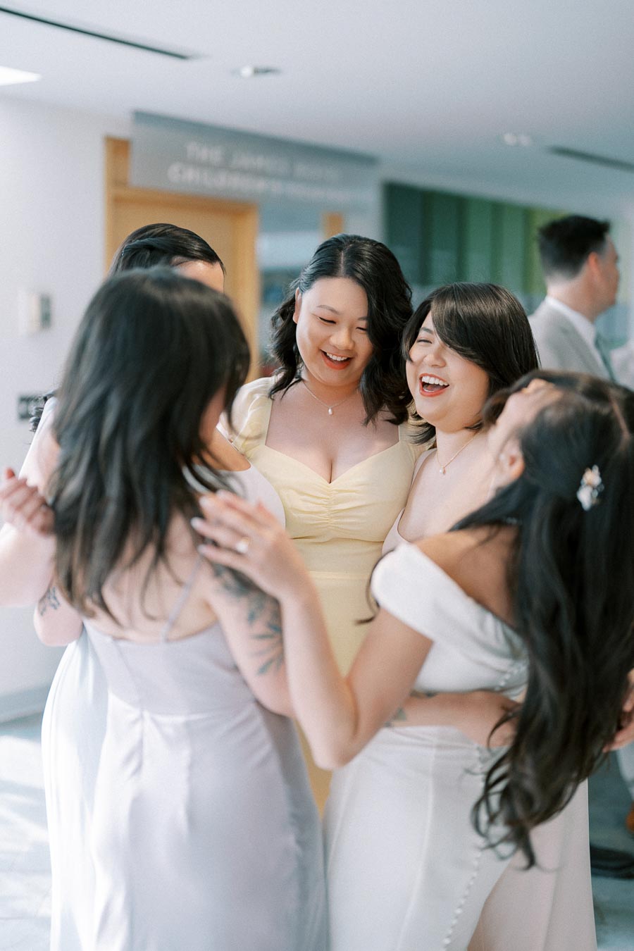 A group of women in elegant dresses smiling and embracing indoors, capturing a joyful moment at a celebration or event.