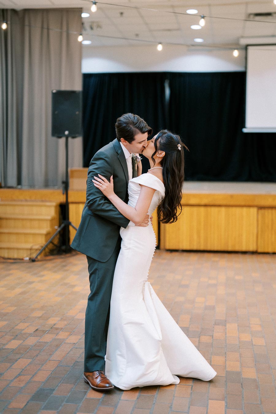 A bride and groom share a romantic kiss on the dance floor at their wedding reception, surrounded by soft lighting and elegant décor.