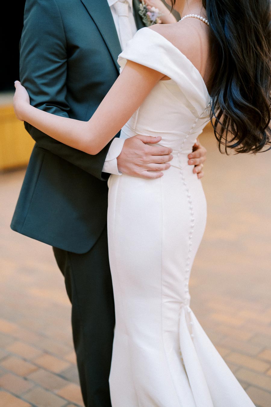 A bride in an elegant white gown embracing her partner wearing a dark suit, capturing a romantic moment on their wedding day.