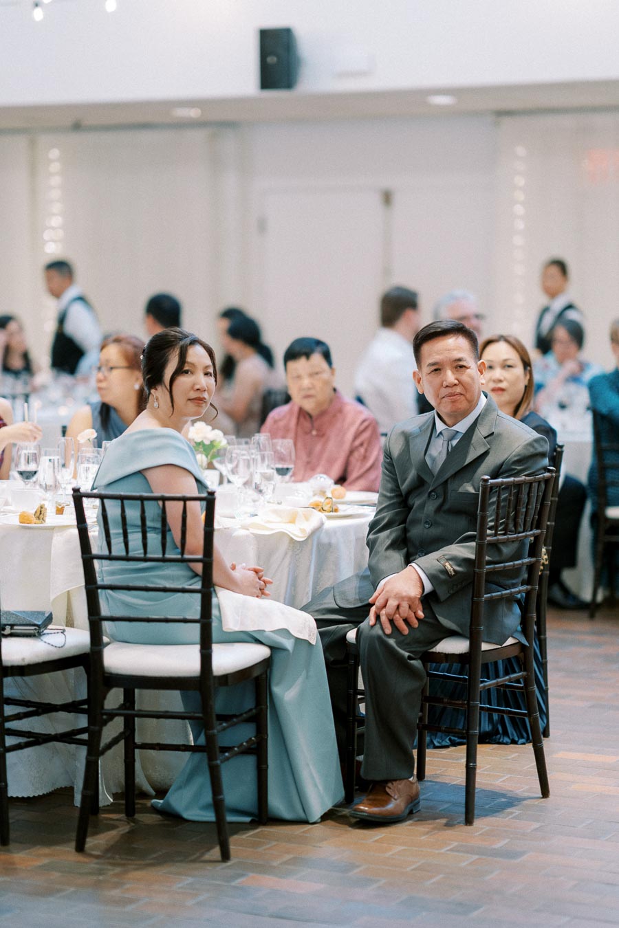 Guests seated at elegantly set tables during a formal event, with individuals wearing formal attire, engaged in conversation and enjoying the occasion.
