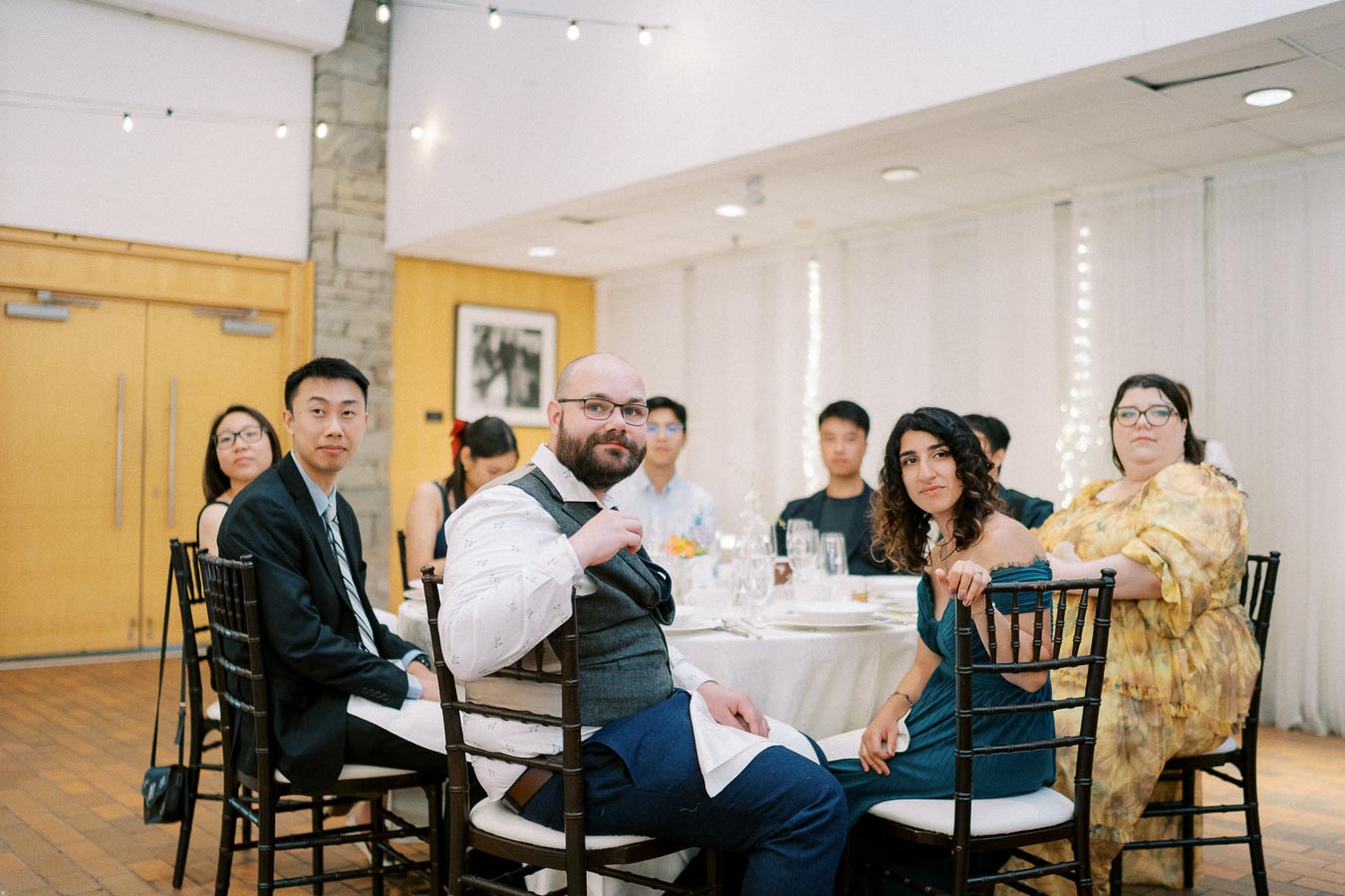 Group of well-dressed people seated around a table at an indoor event, featuring elegant decor and ambient lighting.