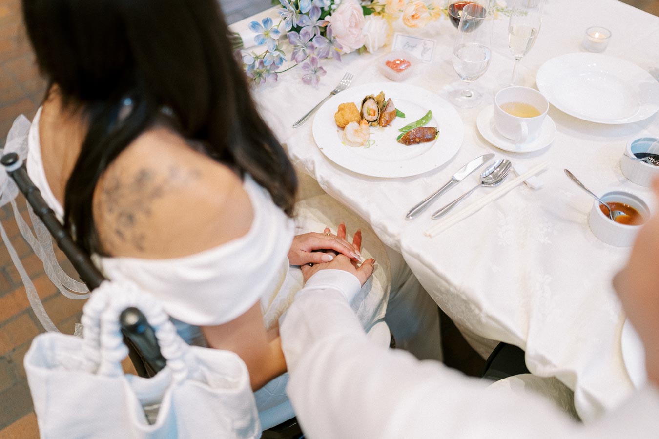 A couple holding hands at an elegantly set table with a gourmet dish and floral centerpiece, showcasing a romantic dining experience.