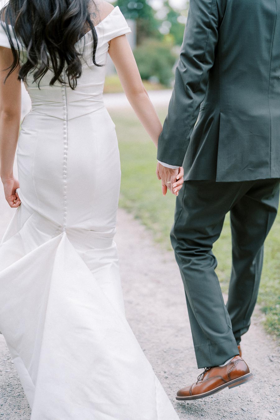 Bride and groom holding hands walking down a path, with the bride in a white wedding dress and the groom in a dark suit, showcasing elegant wedding attire and romantic moment.