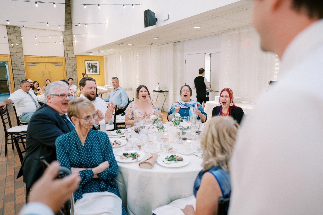 Guests enjoying a lively conversation around a decorated table at a wedding reception, featuring elegant dinner settings and warm lighting.