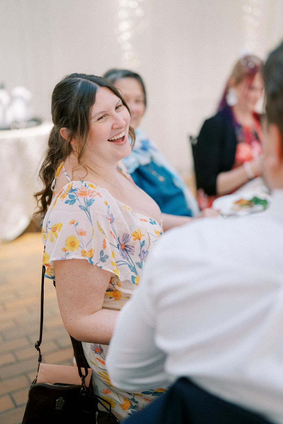 A woman in a floral dress smiling at a social gathering.