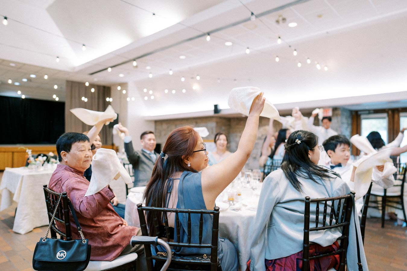 Guests waving napkins in celebration at a wedding reception, showcasing a joyful and festive atmosphere inside a beautifully decorated venue.