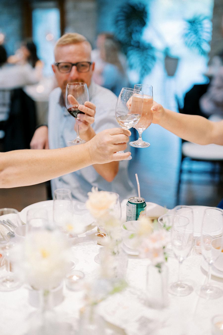 A group of people raising glasses in a toast at an elegant indoor gathering, with beautifully set tables and floral centerpieces.
