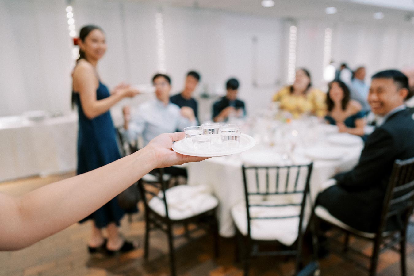 A person in a restaurant serving a plate with shots at a table with smiling guests, creating an atmosphere of celebration and enjoyment.