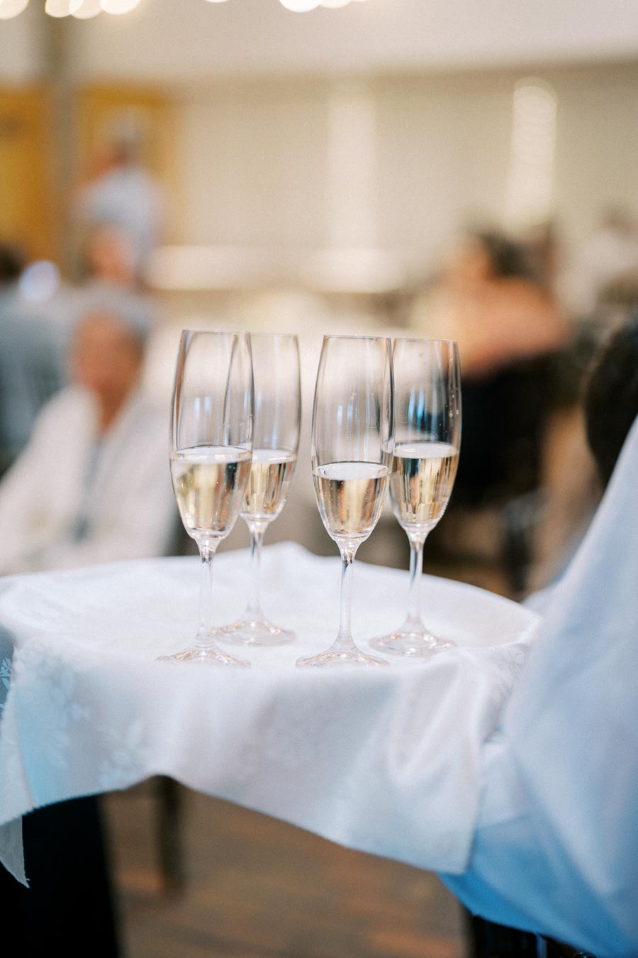 Four filled champagne flutes on a white cloth, carried by a server at an elegant event.