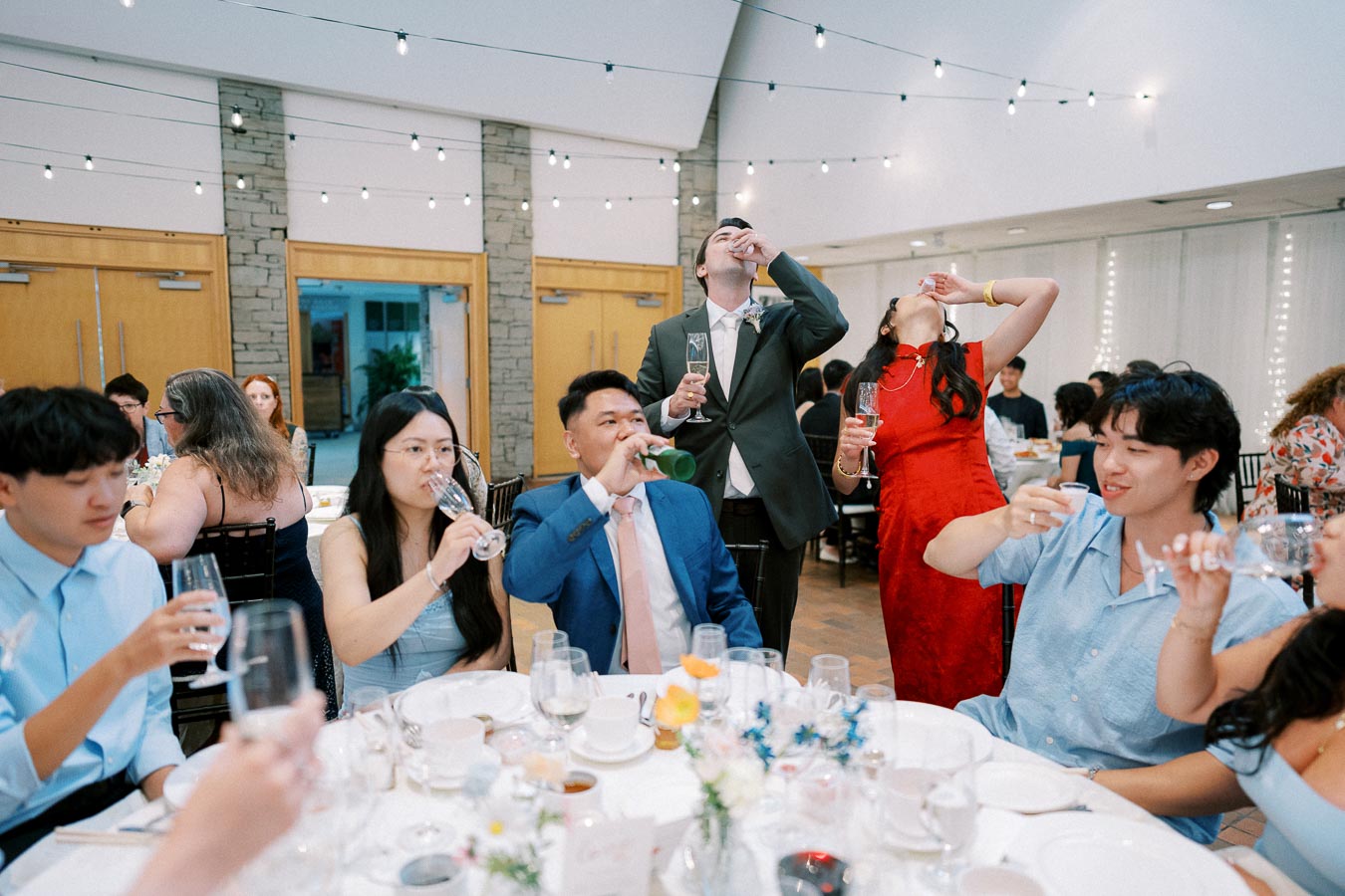 Guests enjoying drinks and celebrating at a vibrant party with festive lighting and elegantly set tables.