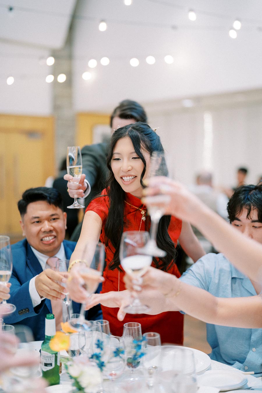 A joyful wedding celebration with guests toasting with champagne glasses around a festive table, under soft ambient lighting.