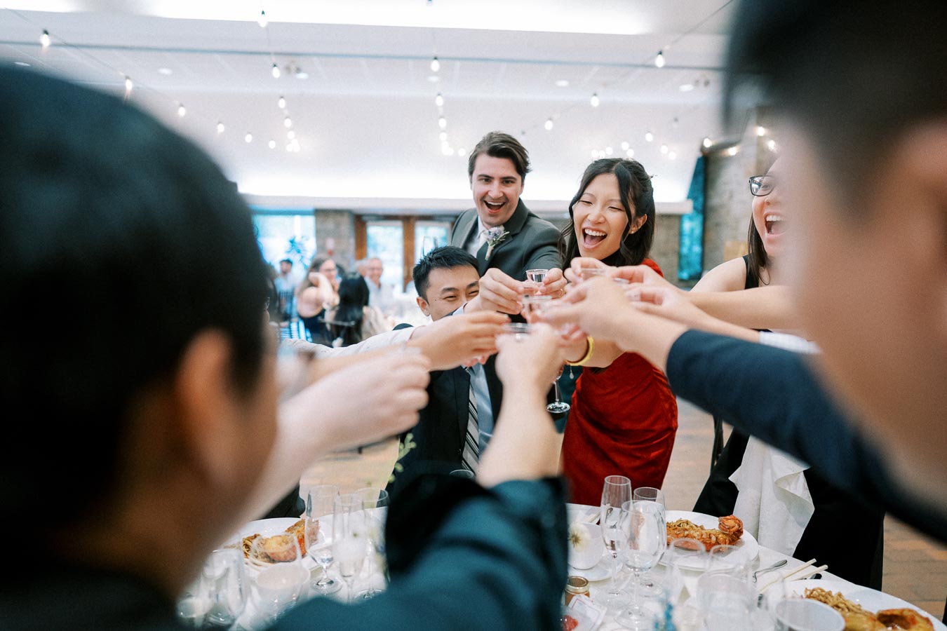 A group of people joyfully toasting at a lively wedding reception, surrounded by elegantly set tables and festive decorations.