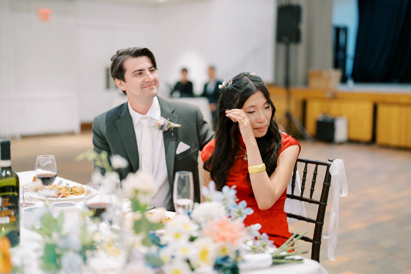 A couple shares an emotional moment at their wedding reception, surrounded by flowers and wine.