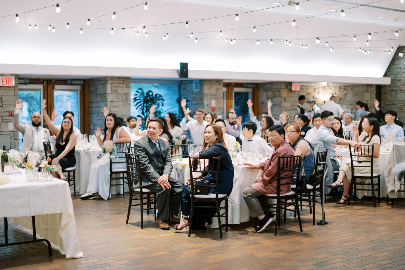 Guests participate in an interactive moment during a formal event, with hands raised in response to a question or activity.