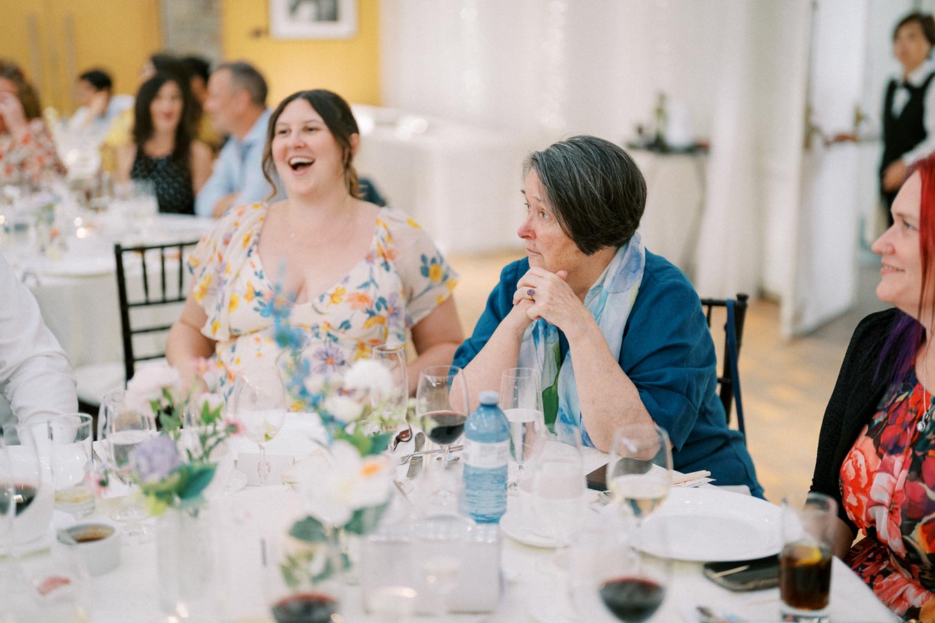 Guests enjoying a lively moment at a formal event, surrounded by elegantly set tables and floral arrangements.