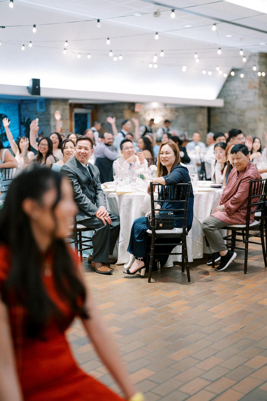 Guests at a wedding reception enjoying the event, seated around tables with string lights overhead.